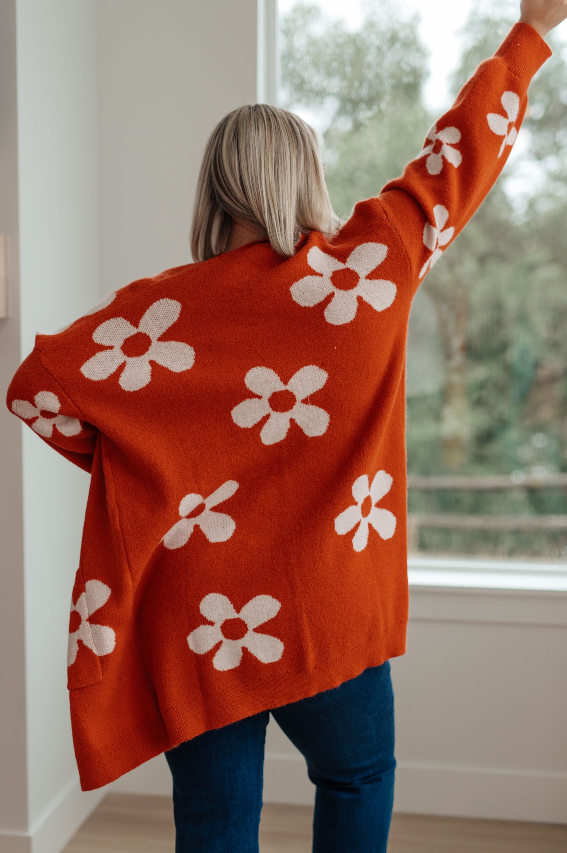 Person wearing an orange sweater with white floral patterns, standing indoors.