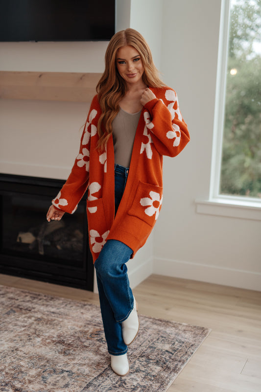 Woman wearing an orange cardigan with white floral patterns in a living room.