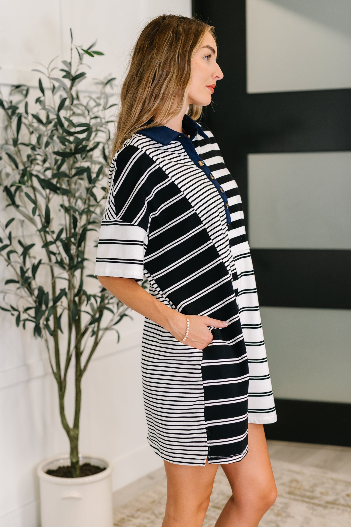 Woman wearing a black and white striped dress standing next to a potted plant indoors.