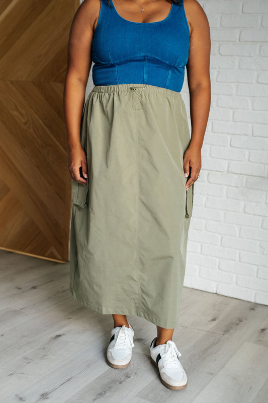 Person wearing a blue top and green skirt standing against a white brick wall.