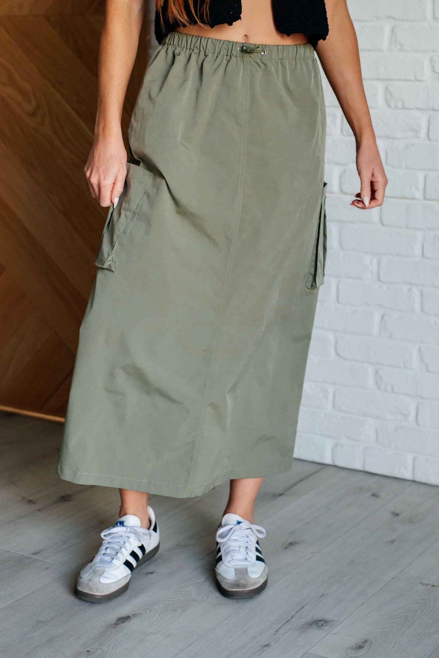 Person wearing a green skirt and white sneakers against a white brick wall.