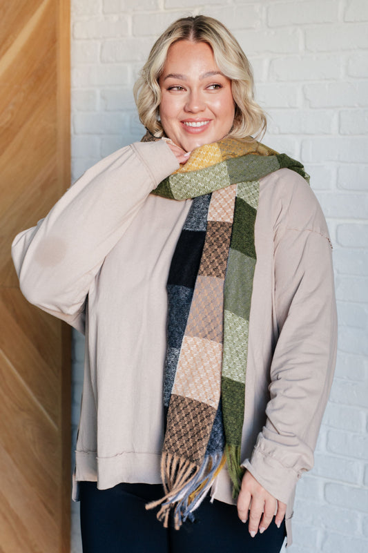 Woman wearing a patchwork scarf against a white brick wall.