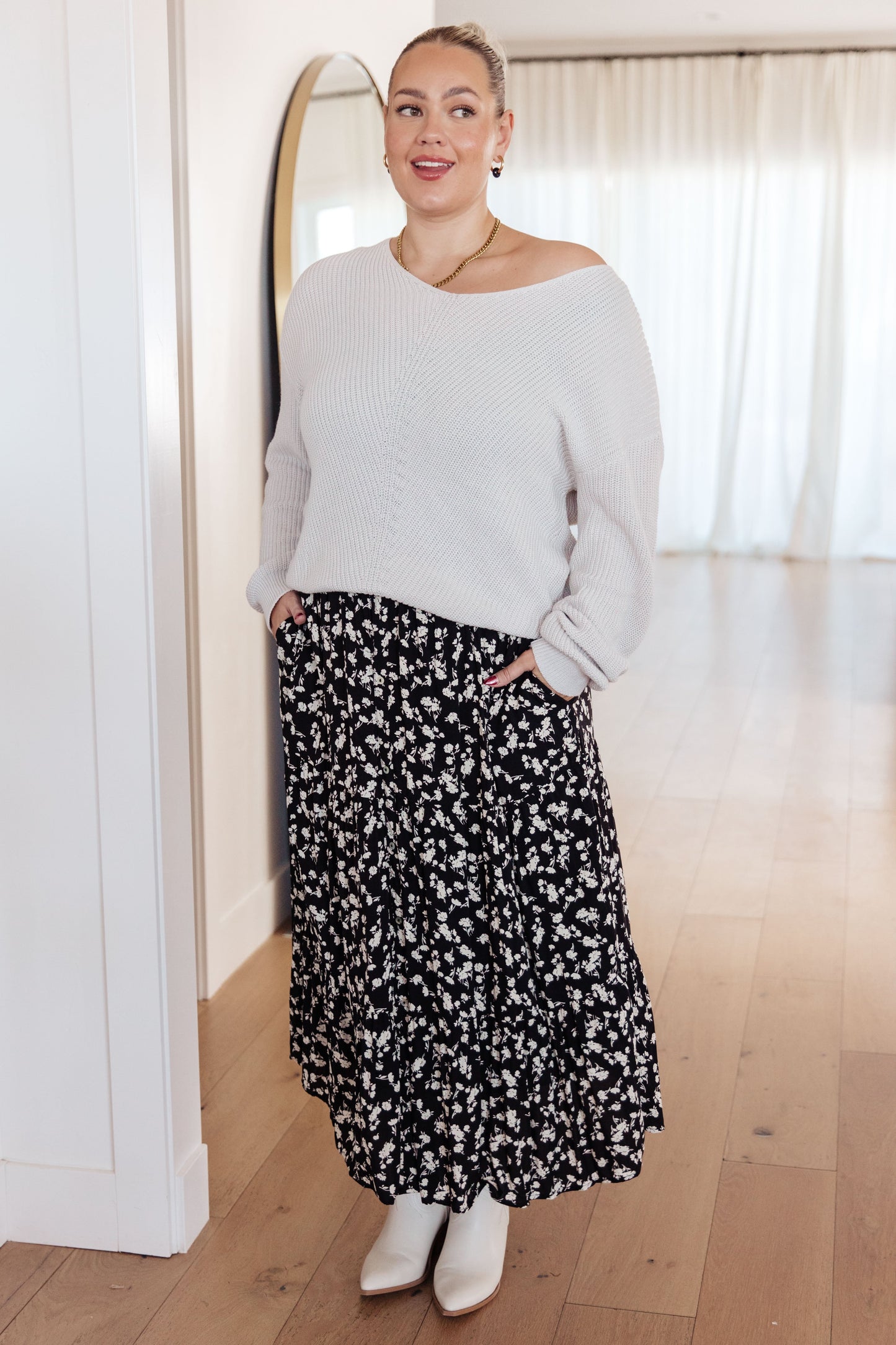 Woman wearing a light gray sweater and black floral skirt indoors.