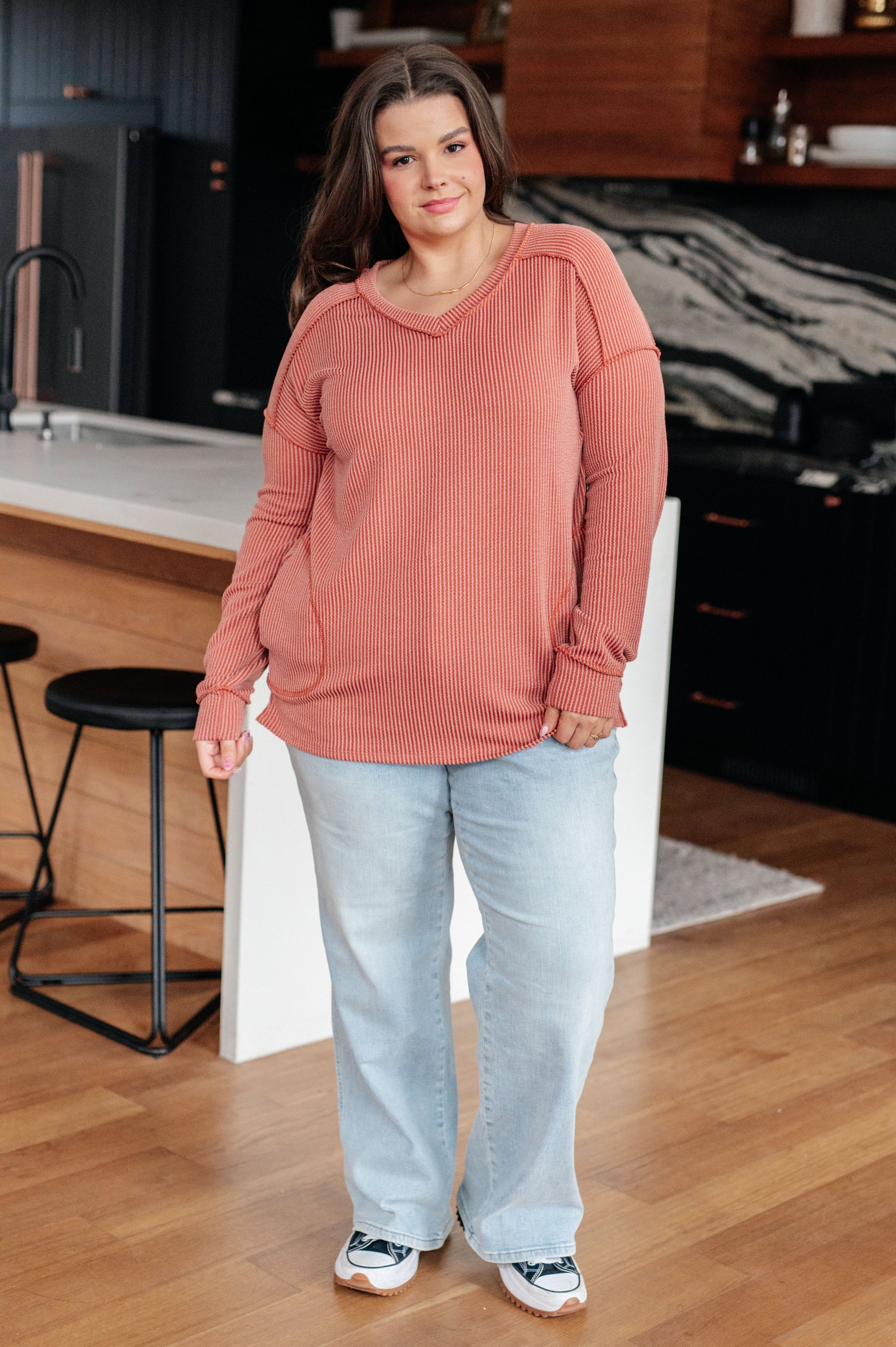 Woman wearing a pink sweater and light blue jeans standing in a kitchen.