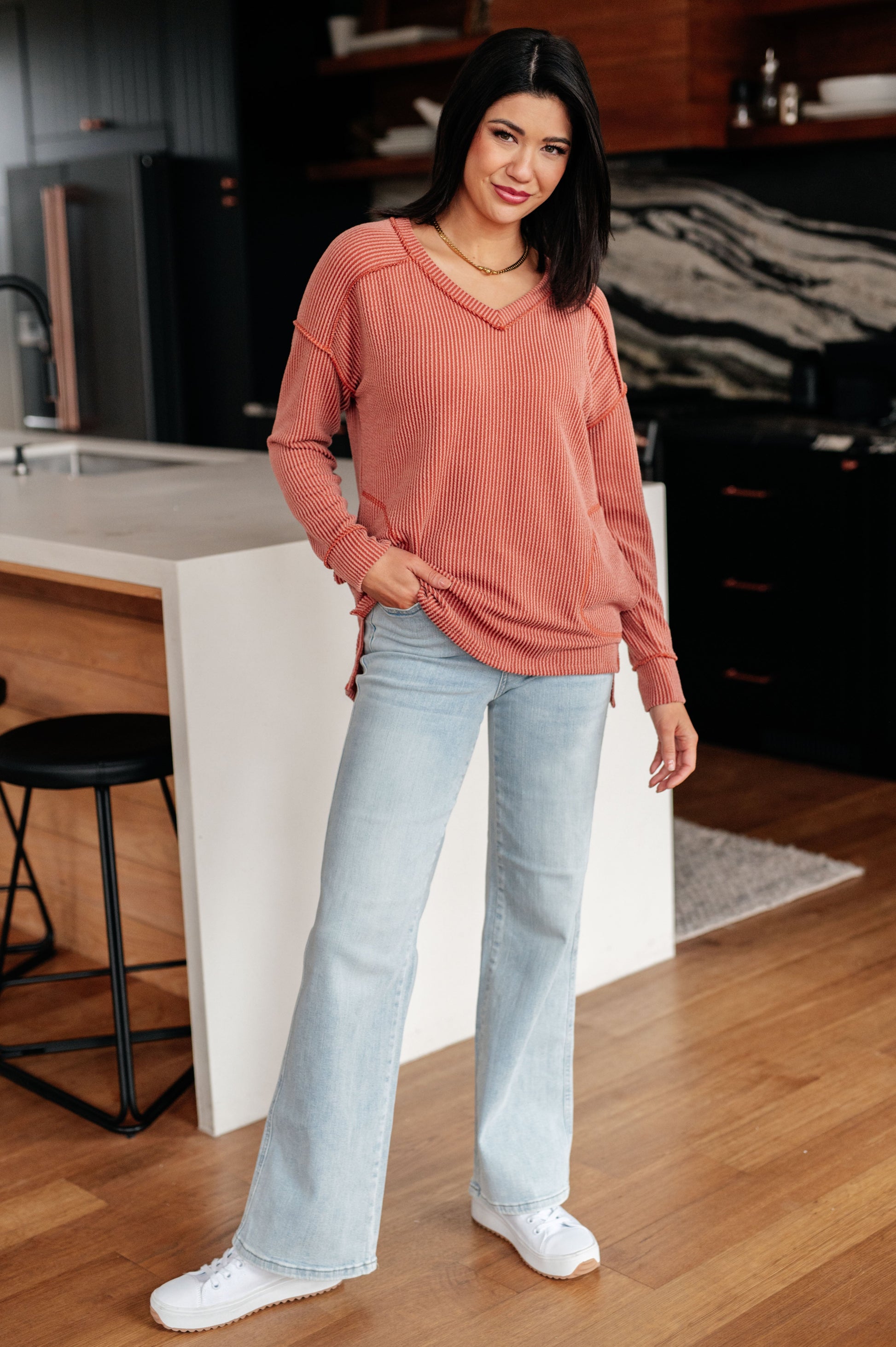 Woman wearing a pink sweater and light blue jeans standing in a kitchen.