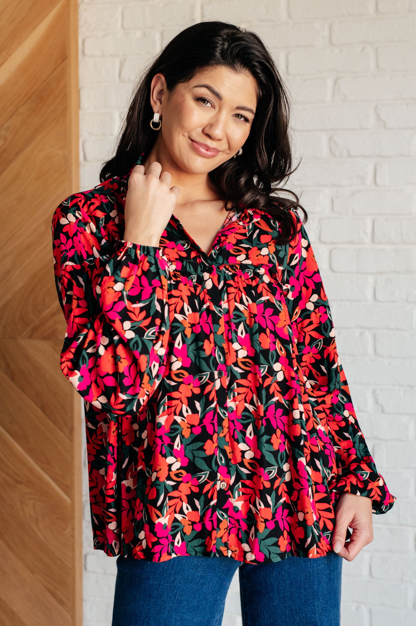 Woman wearing a colorful floral blouse against a white brick wall.