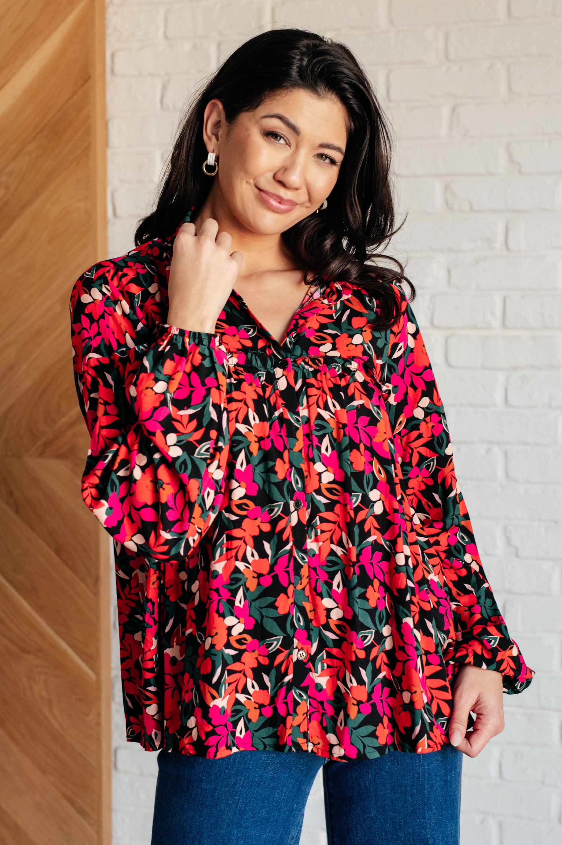 Woman wearing a colorful floral blouse against a white brick wall.