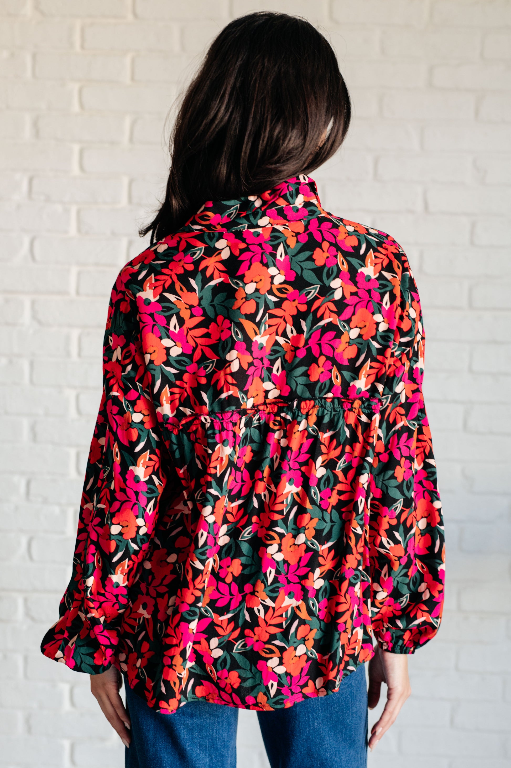 Person wearing a colorful floral blouse against a white brick wall.