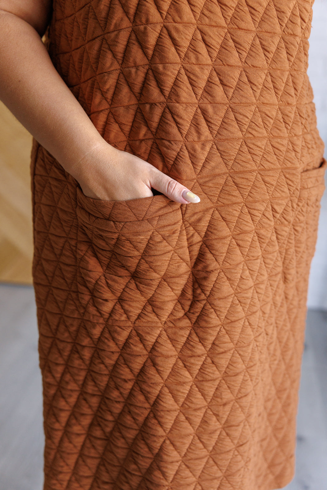 Brown quilted dress with a hand in the pocket against a neutral background