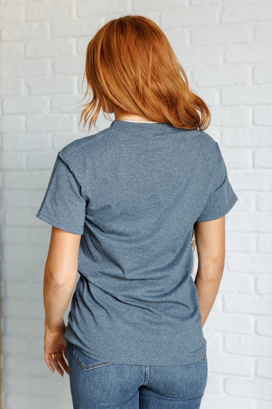 Person wearing a blue t-shirt and jeans against a white brick wall