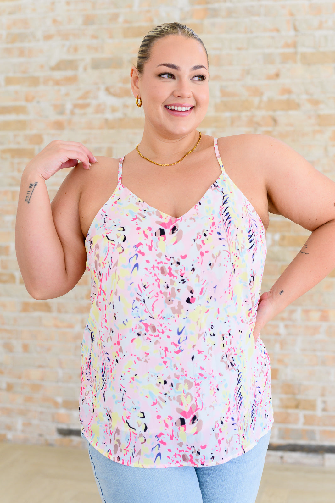 A woman wearing a multicolor printed camisole top with a v-neckline and adjustable straps, paired with high-rise straight jeans.