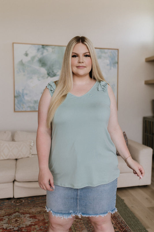 Woman wearing a light green sleeveless top and denim shorts in a living room.