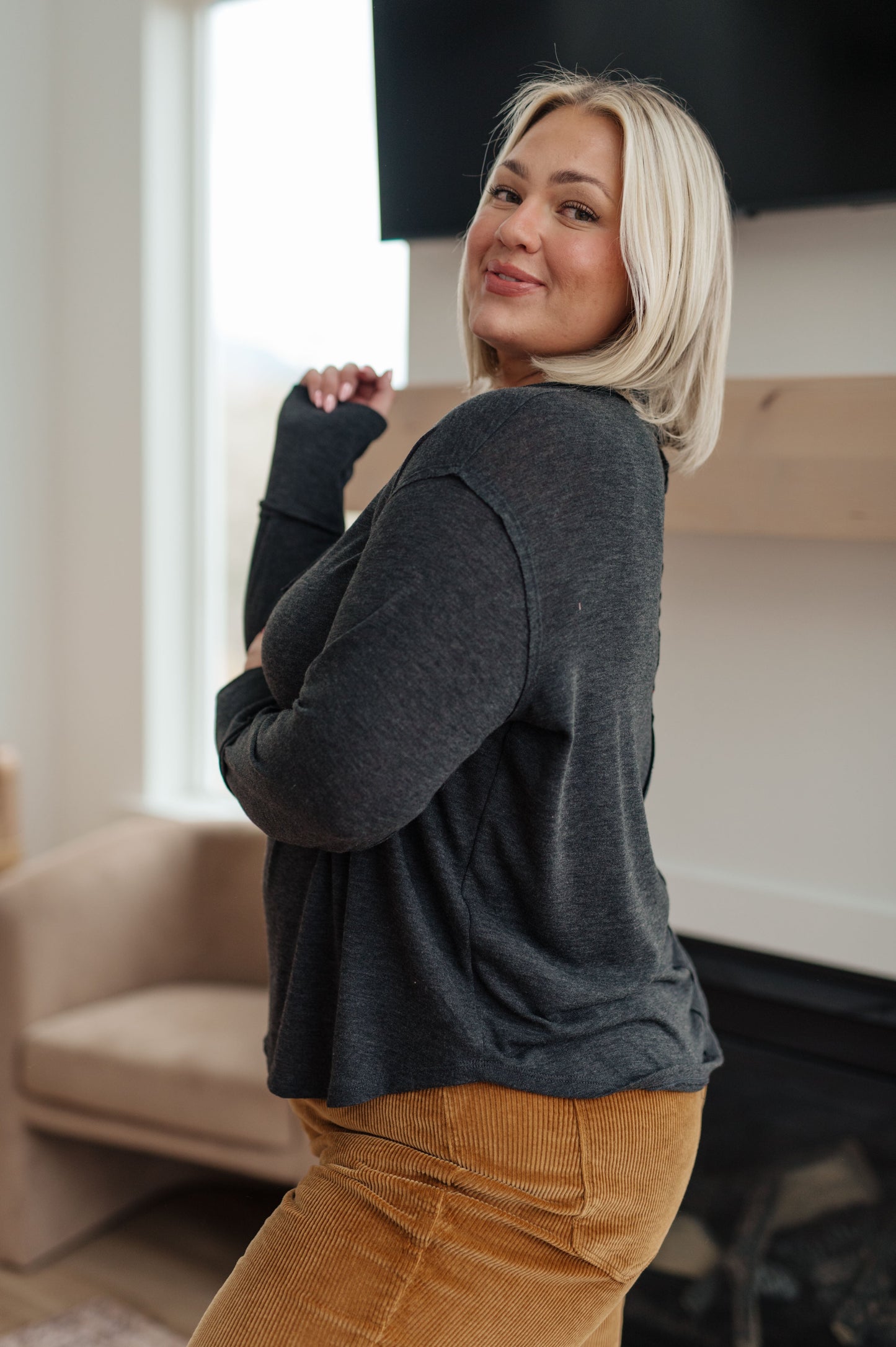 Woman wearing a dark gray sweater and tan pants in a living room setting.
