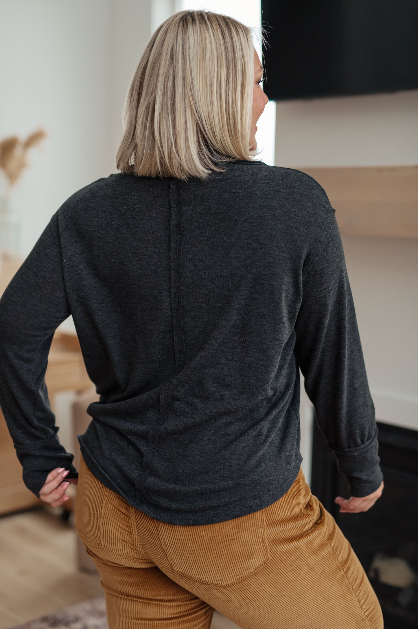 Person wearing a dark gray long-sleeve shirt and brown pants in an indoor setting.