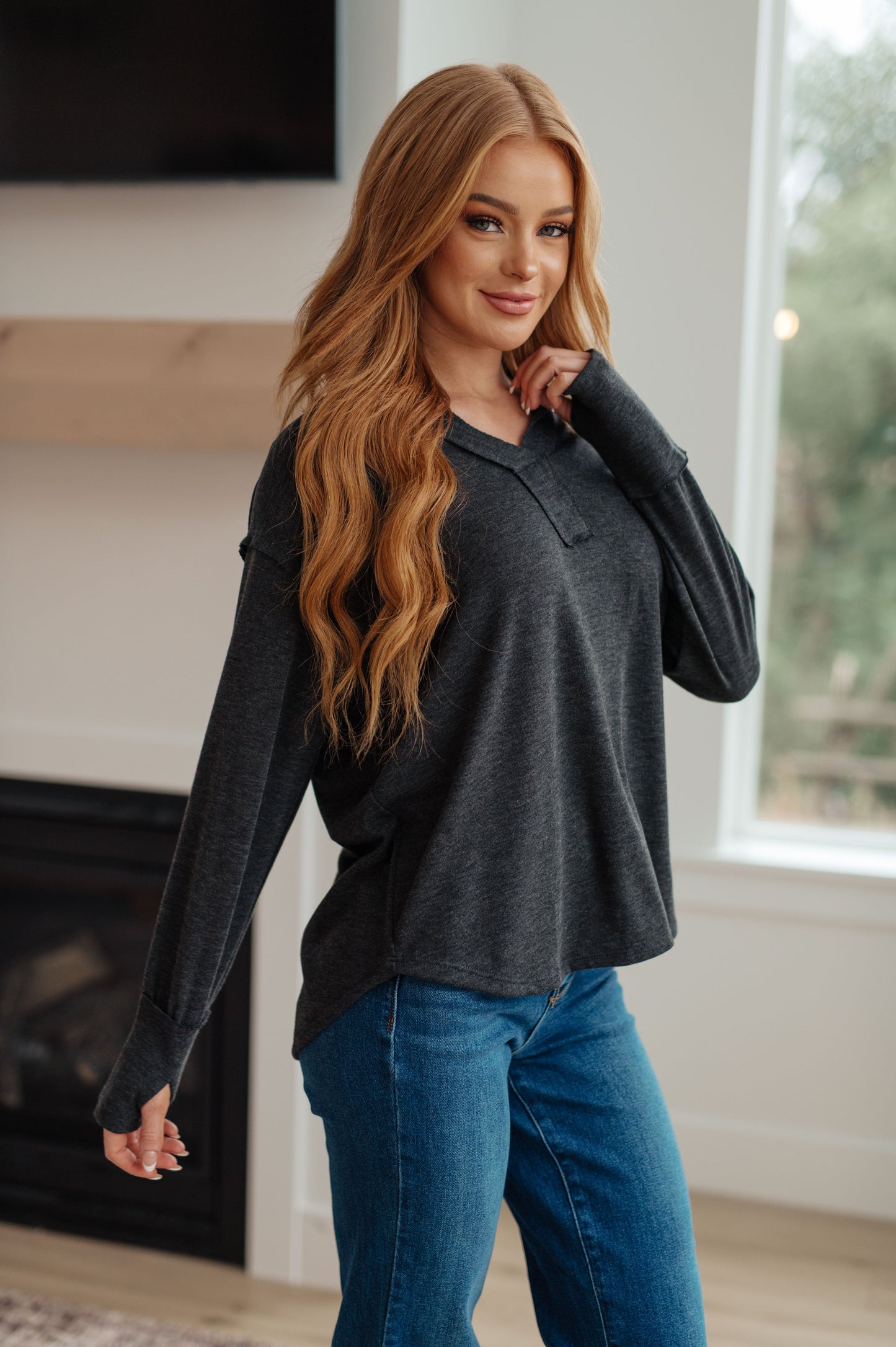 Woman wearing a dark long-sleeve top and blue jeans indoors.