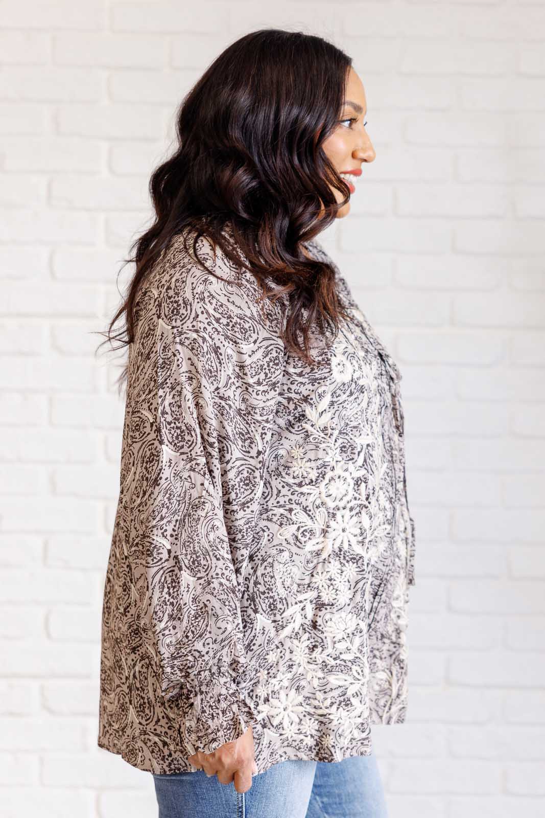 Woman wearing a patterned blouse against a white brick wall