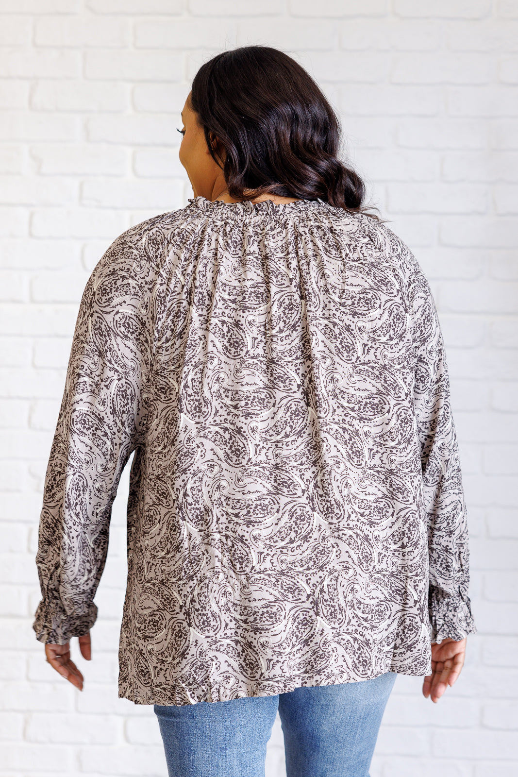 Woman wearing a patterned blouse against a white brick wall