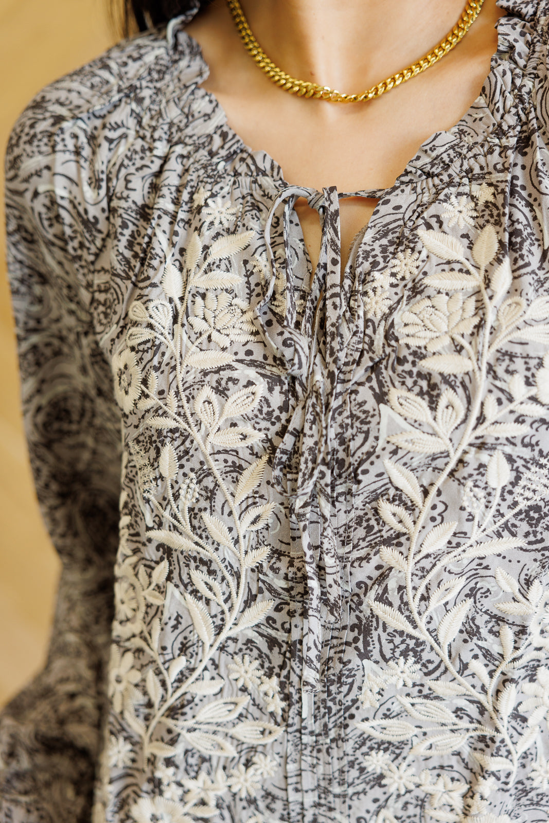 Close-up of a patterned blouse with a gold necklace on a neutral background