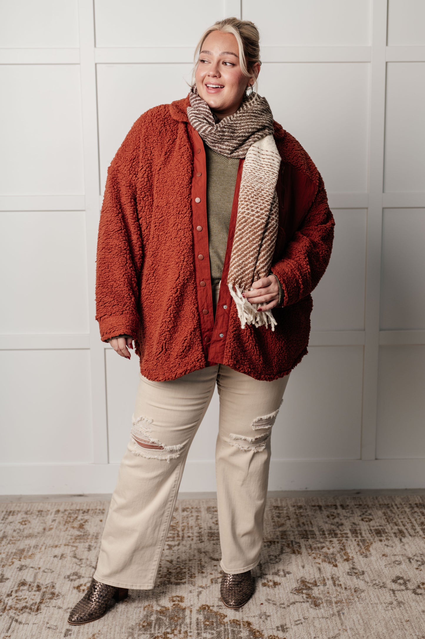 Person wearing a red jacket, beige scarf, and beige pants against a white wall.