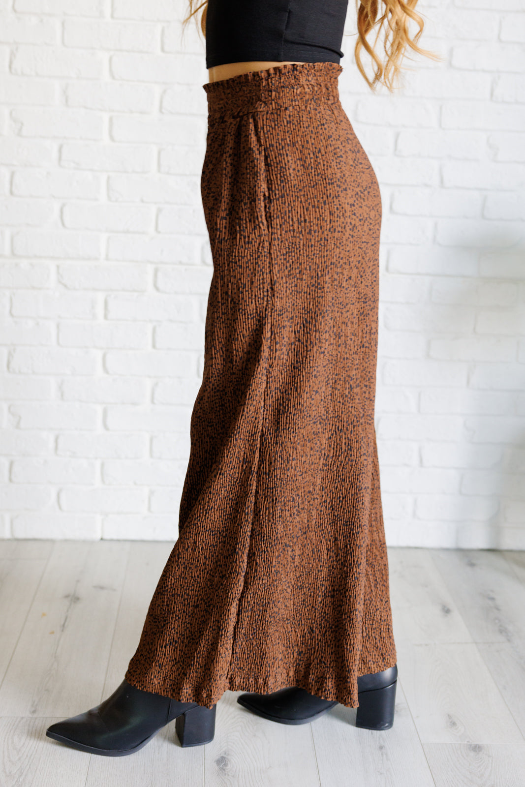 Brown textured pants worn by a person against a white brick wall.