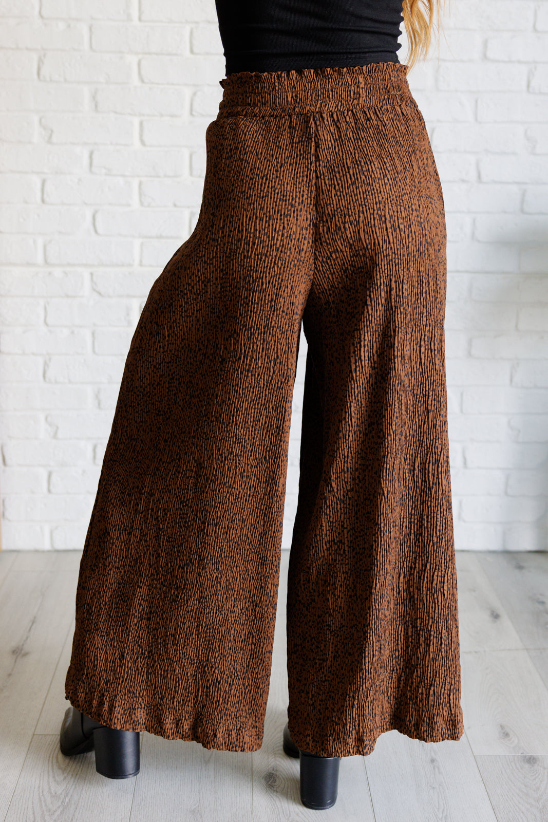 Brown textured wide-leg pants worn by a person against a white brick wall.