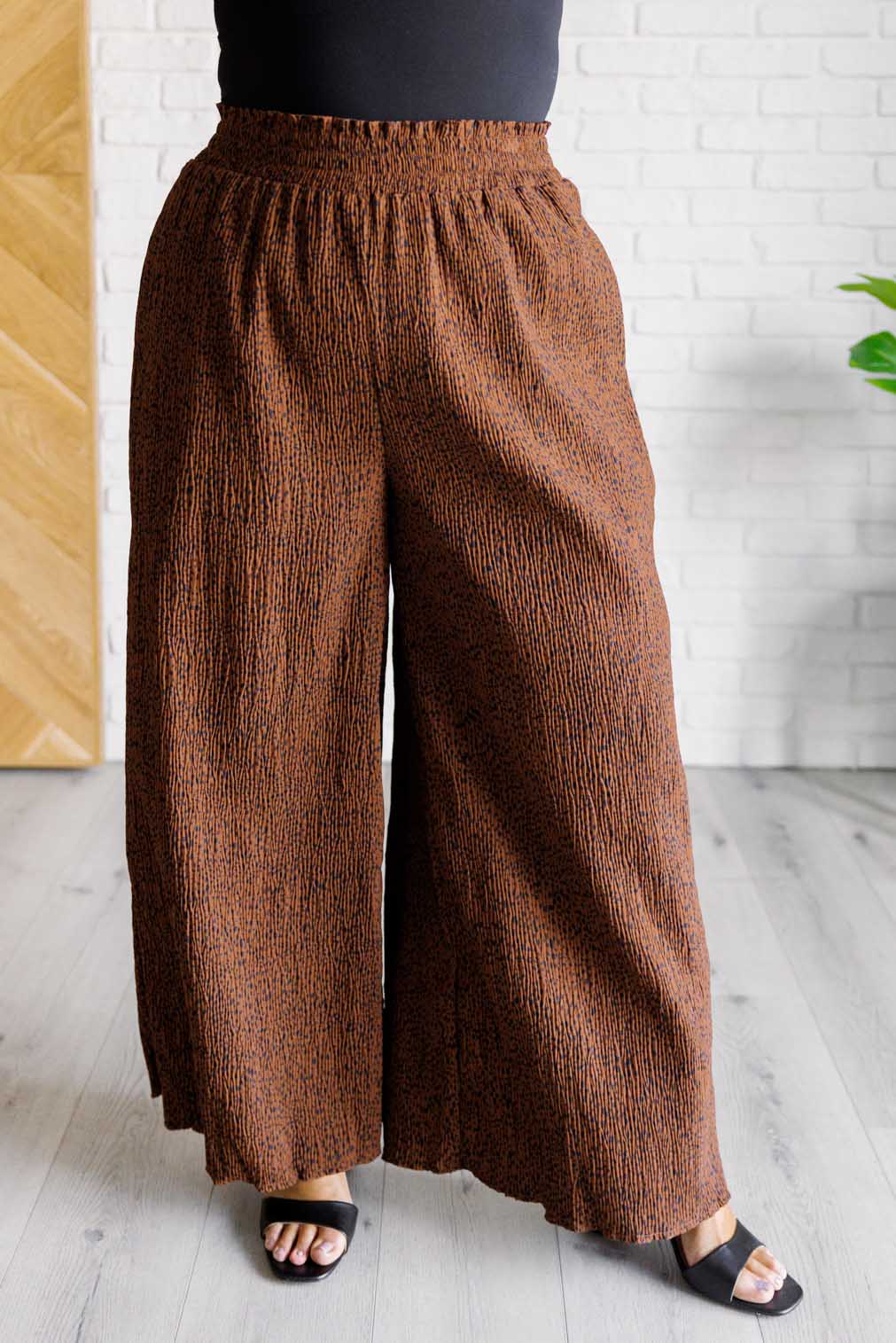 Brown textured wide-leg pants worn by a person against a white brick wall.