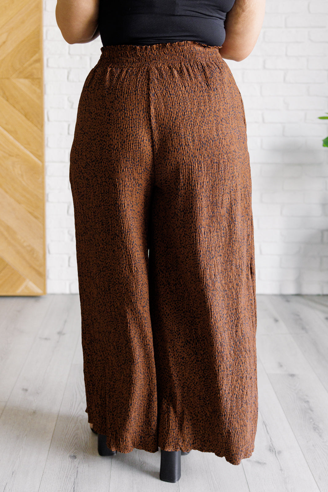 Brown wide-leg pants worn by a person against a white brick wall.