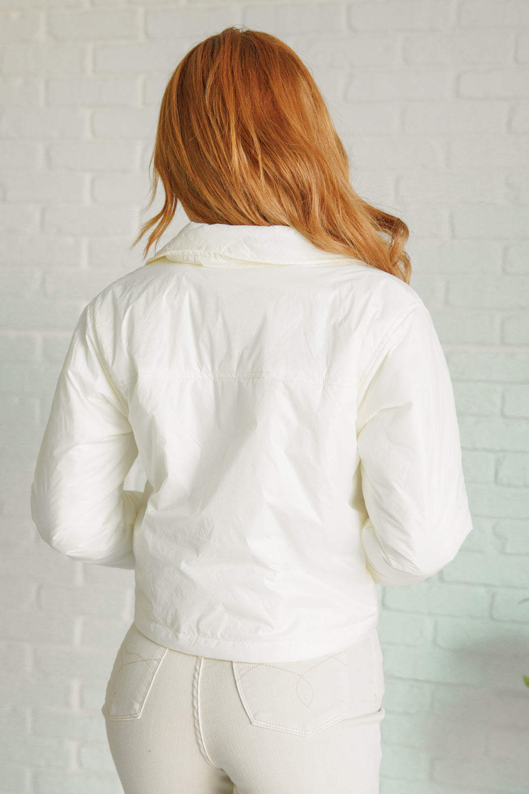 Person wearing a white jacket against a light brick wall