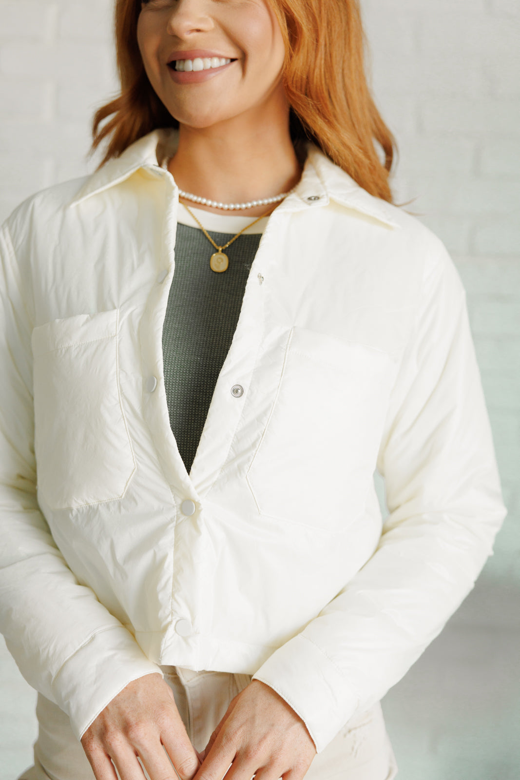 Woman wearing a white puffer jacket over a green top against a light background