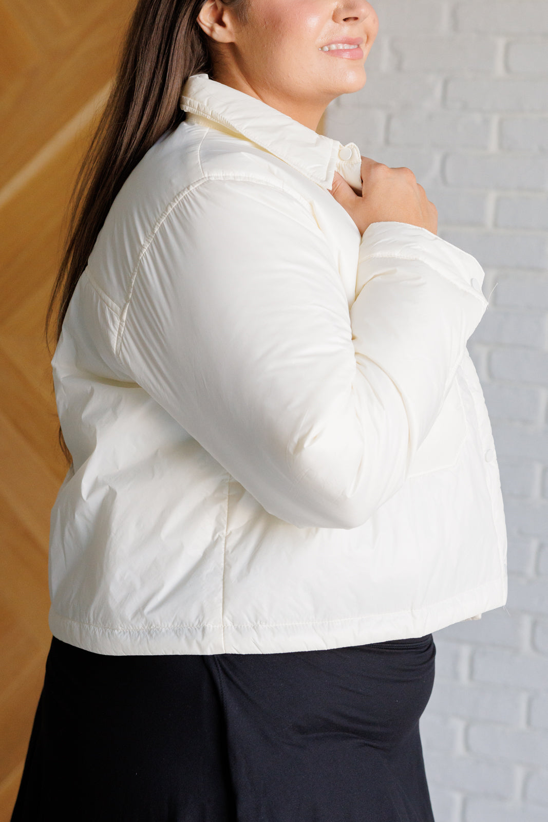 Woman wearing a white puffer jacket against a light brick wall.
