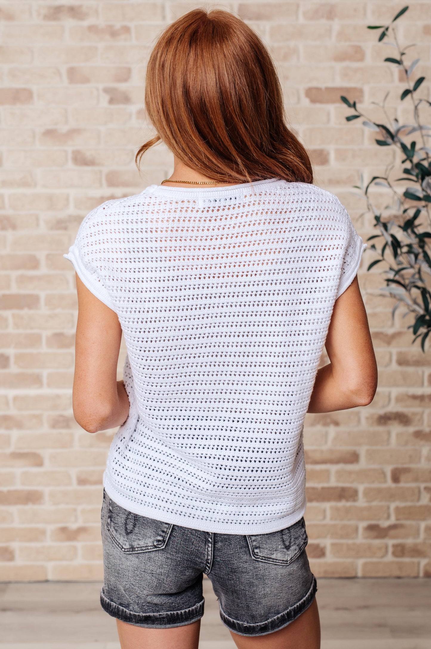 Woman wearing a white crochet top and denim shorts against a brick wall.