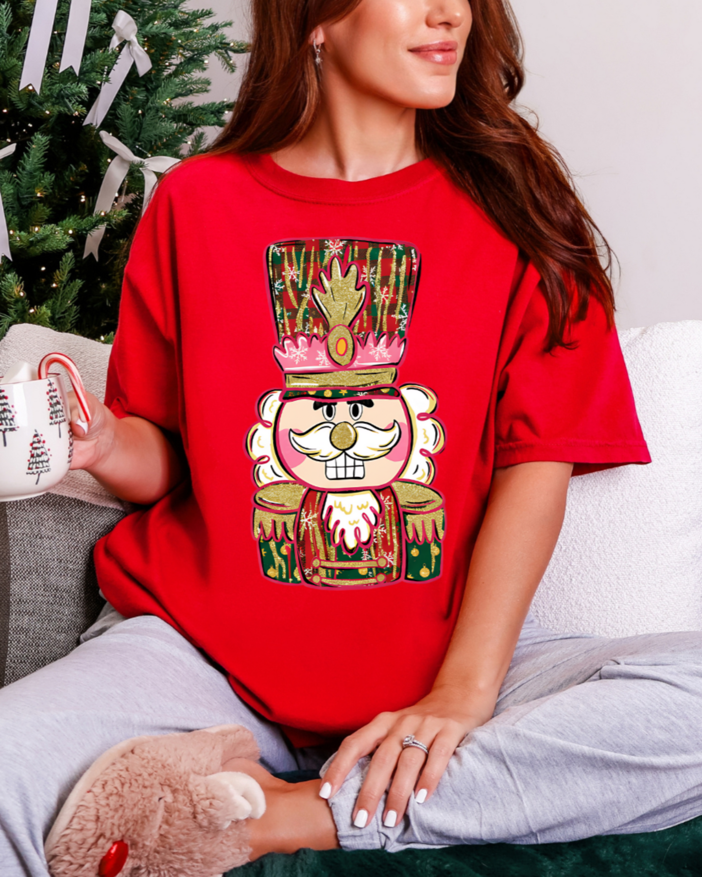 Person wearing a red t-shirt with a festive design, sitting in front of a Christmas tree.