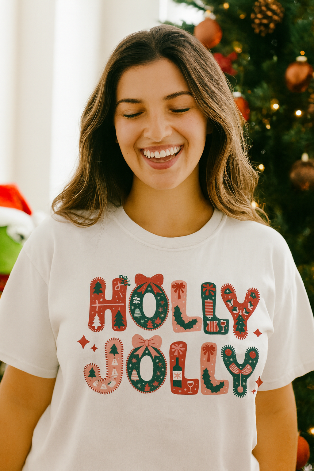 Woman wearing a 'Holly Jolly' shirt in front of a decorated Christmas tree.