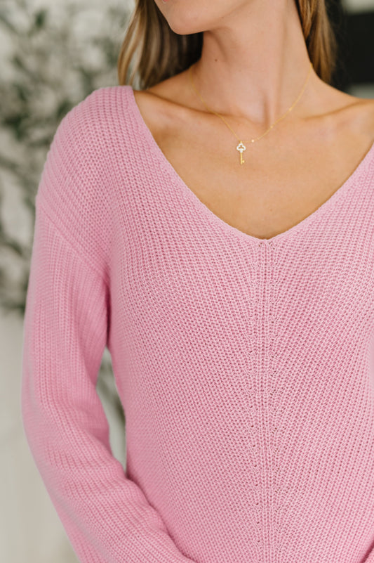 Person wearing a pink sweater with a gold necklace featuring a key pendant.