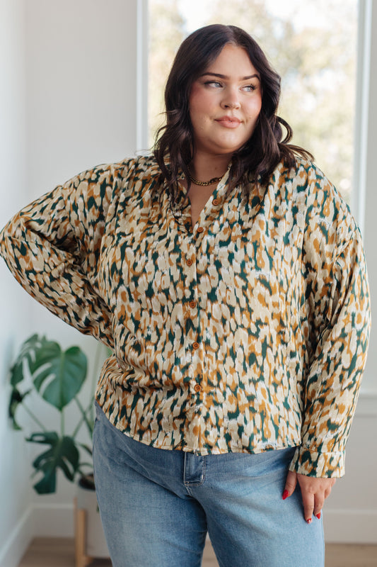 Woman wearing a patterned blouse and jeans indoors with a plant in the background