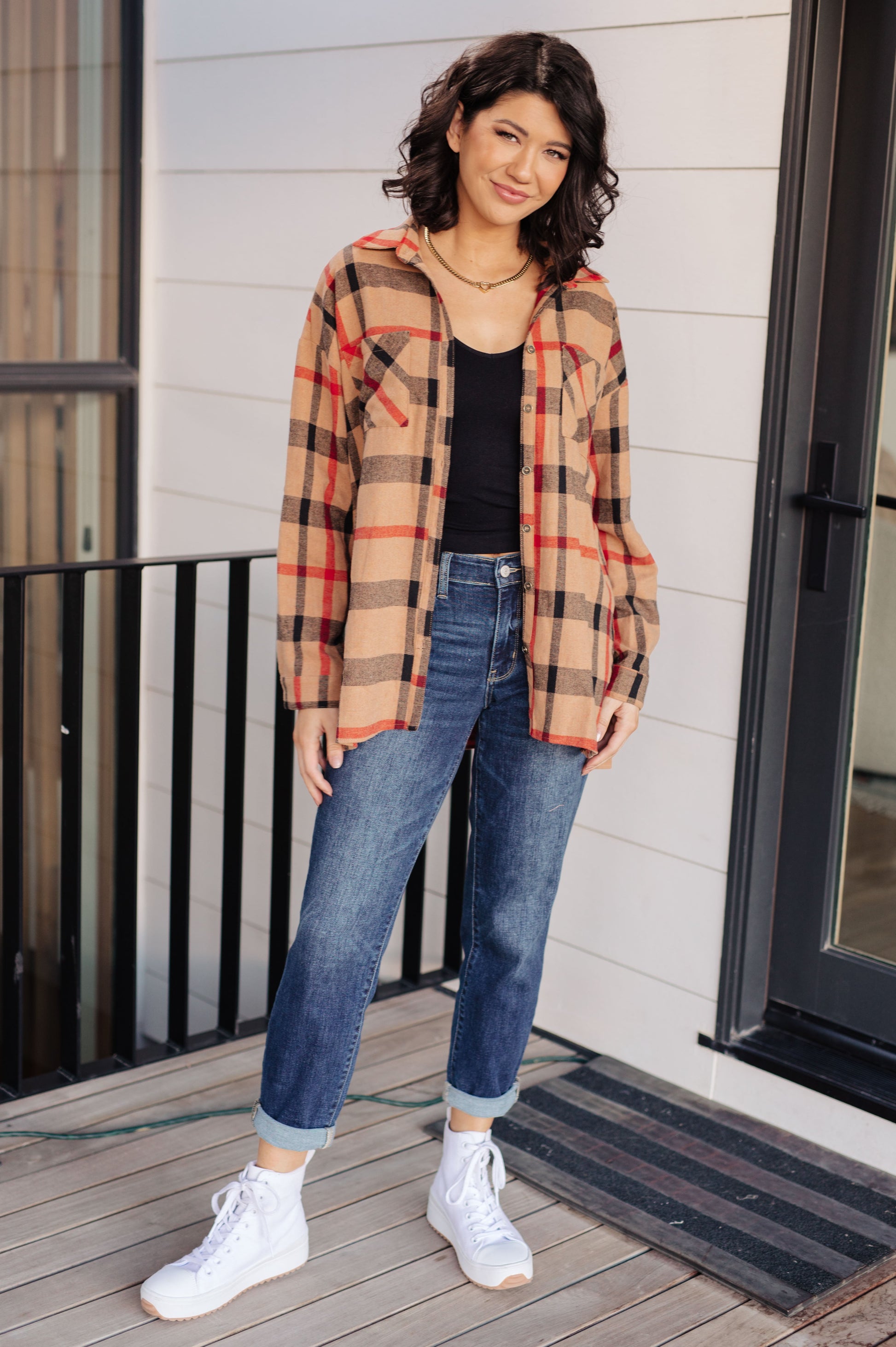 Woman wearing a plaid shirt, jeans, and white sneakers on a wooden deck.