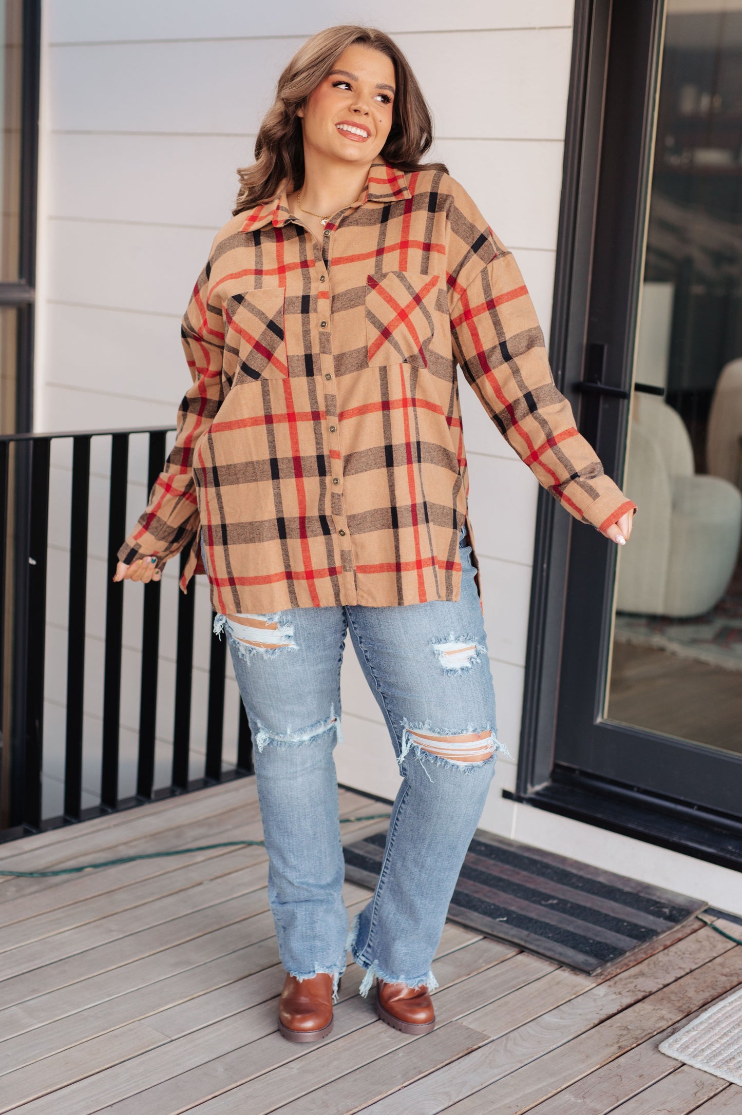 Woman wearing a plaid shirt and jeans standing on a wooden deck.