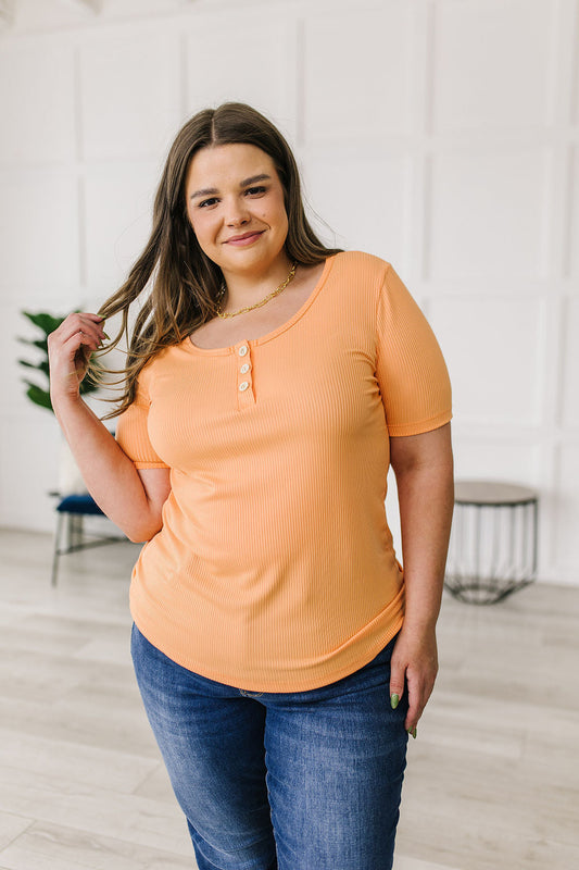 Woman wearing an orange top and blue jeans indoors.
