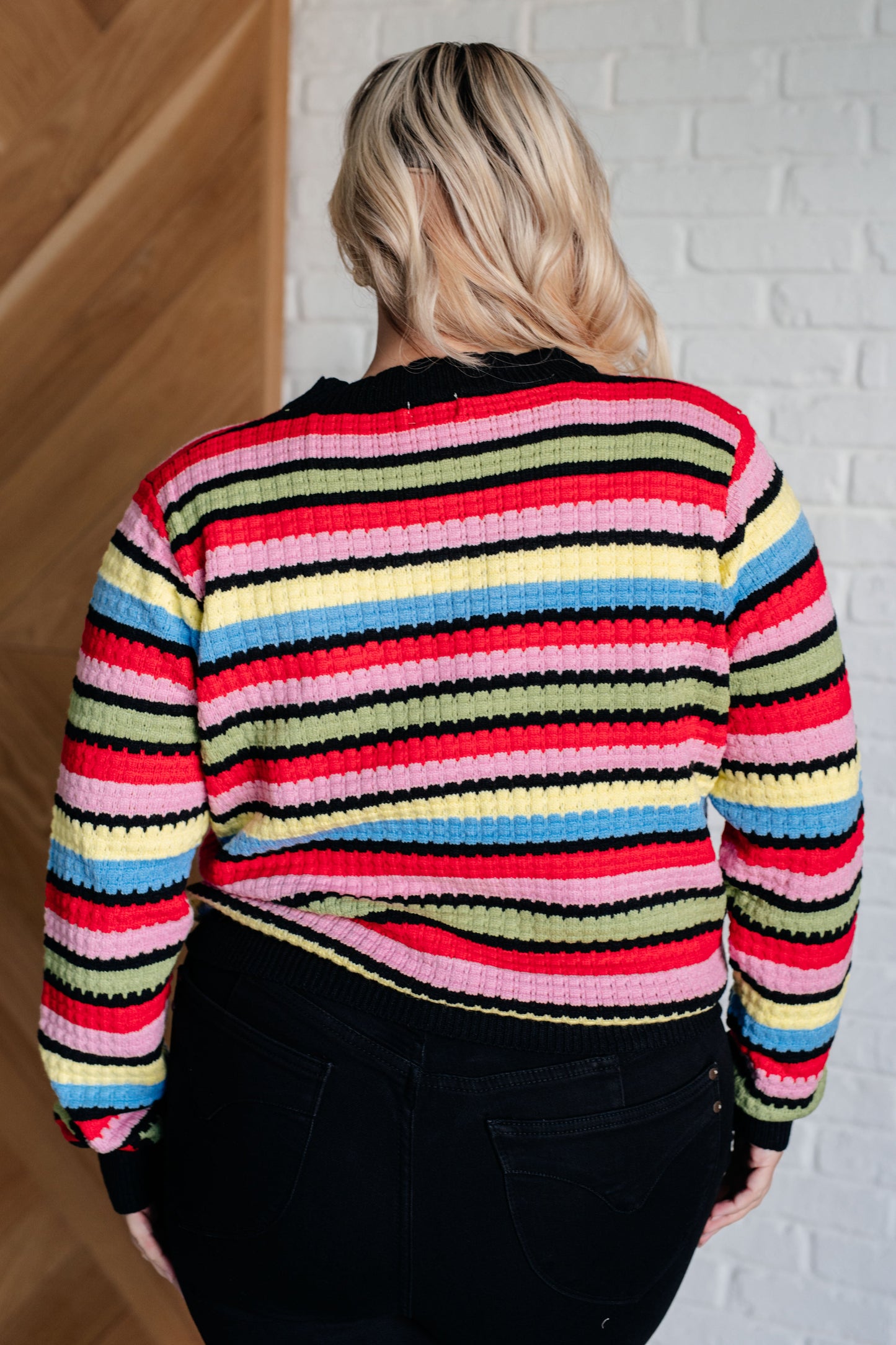 Person wearing a colorful striped sweater in front of a white brick wall.
