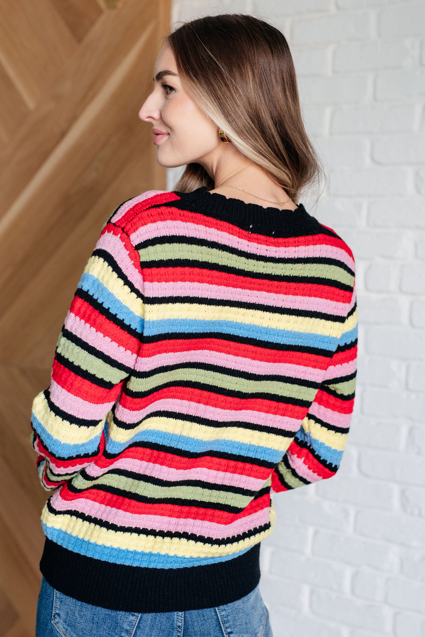 Woman wearing a colorful striped sweater against a white brick wall.