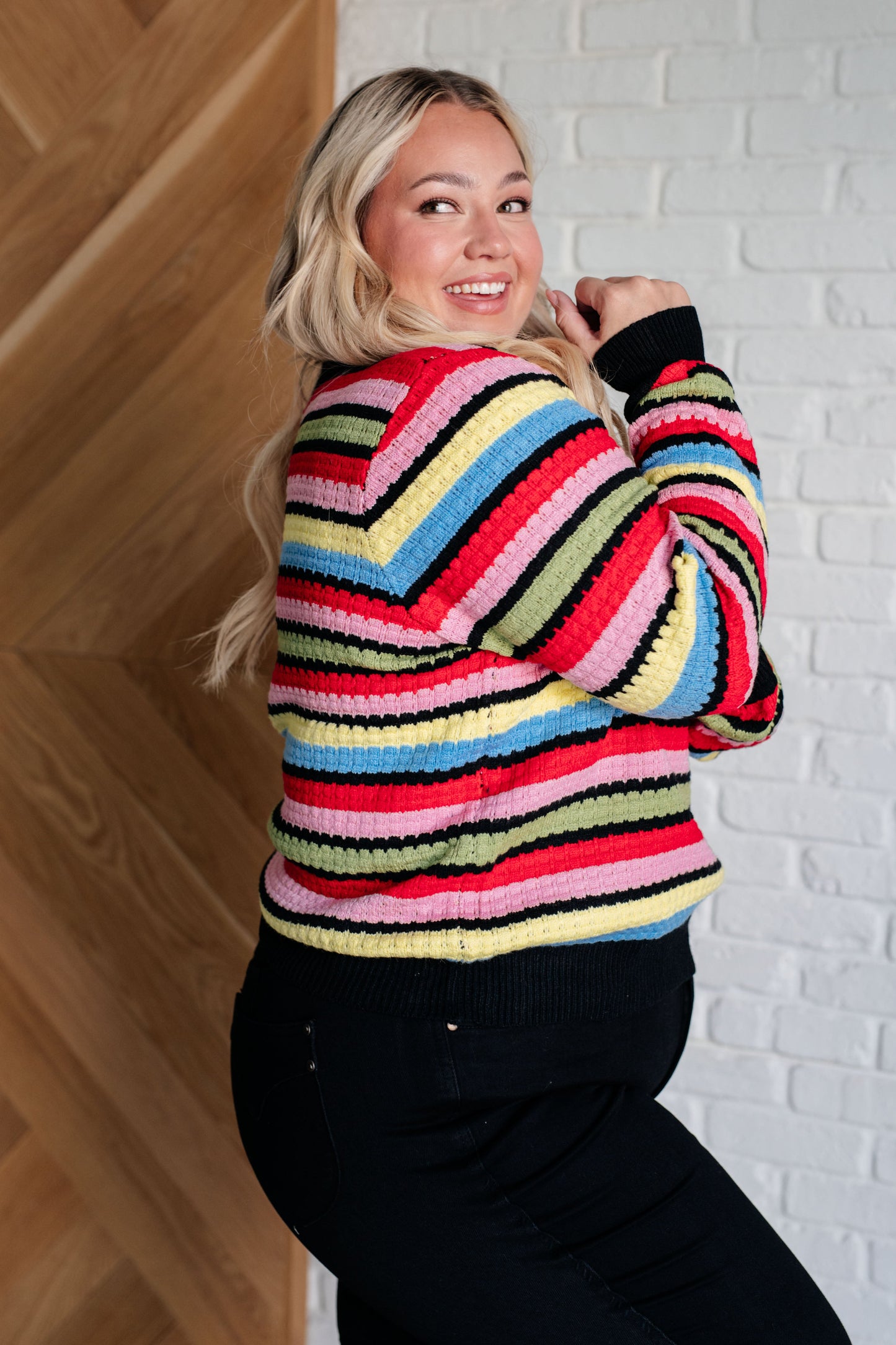 Woman wearing a colorful striped sweater against a white brick wall.