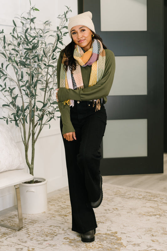 Woman wearing a green sweater, black pants, and a colorful scarf indoors.