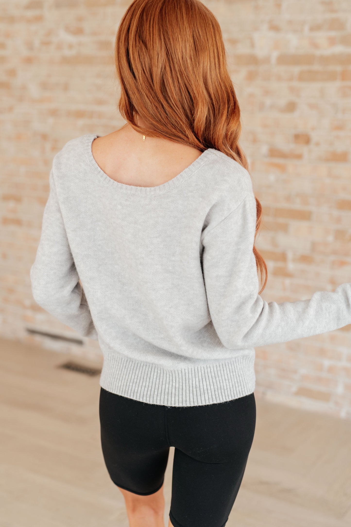 Person wearing a gray sweater and black shorts against a brick wall.