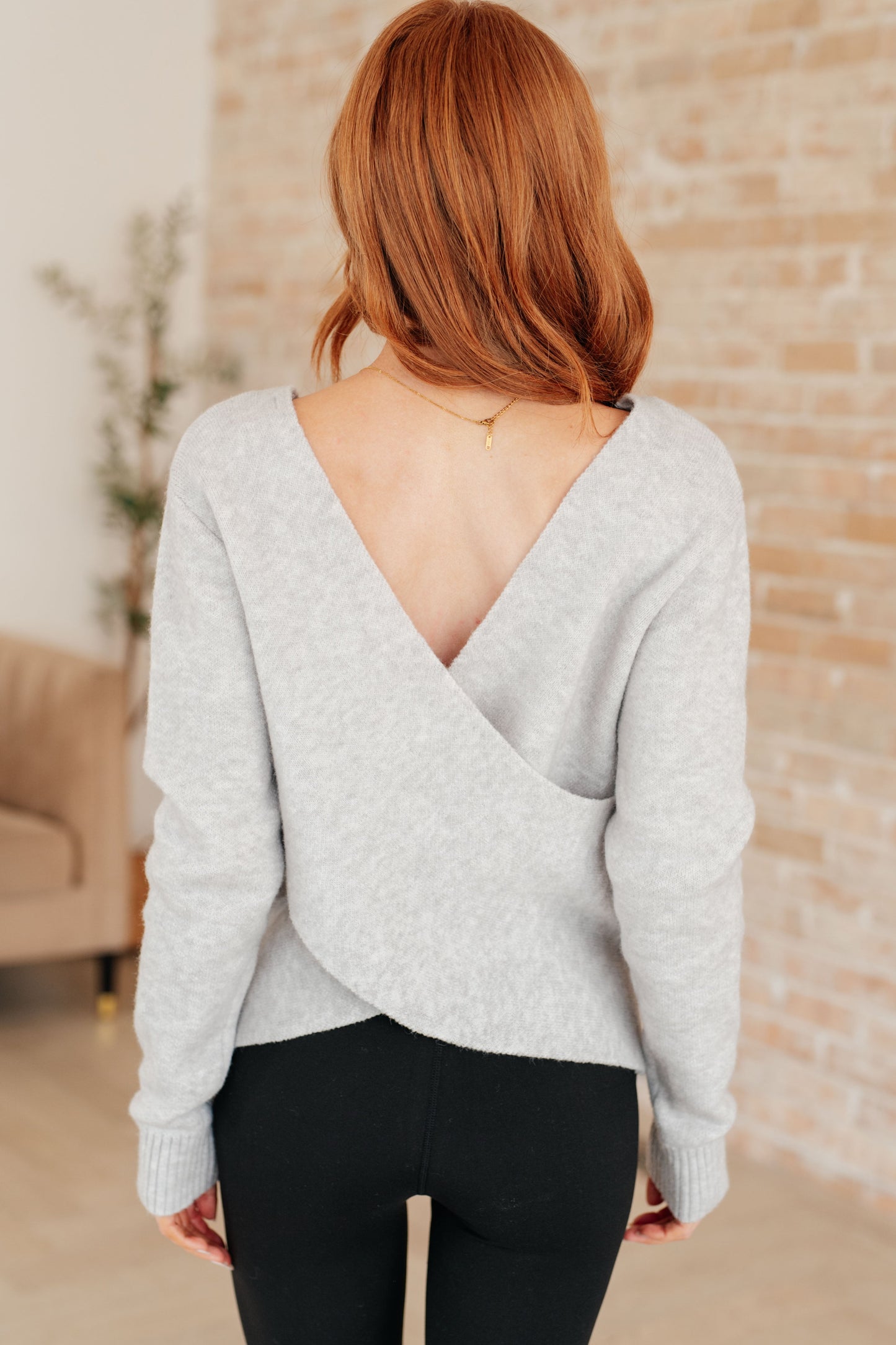 Woman wearing a light gray sweater with an open back in a casual indoor setting.