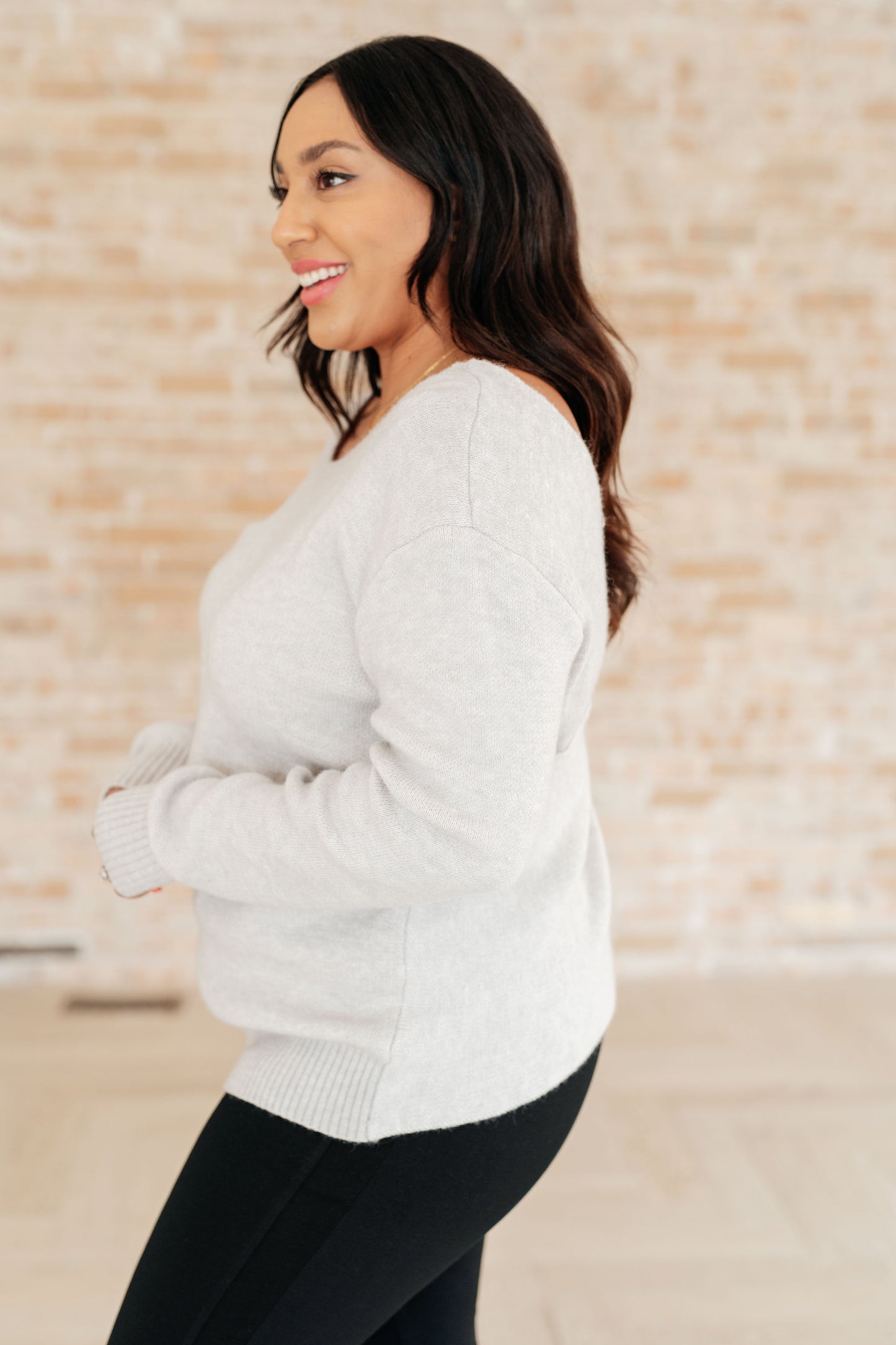 Woman wearing a light gray sweater against a beige brick wall