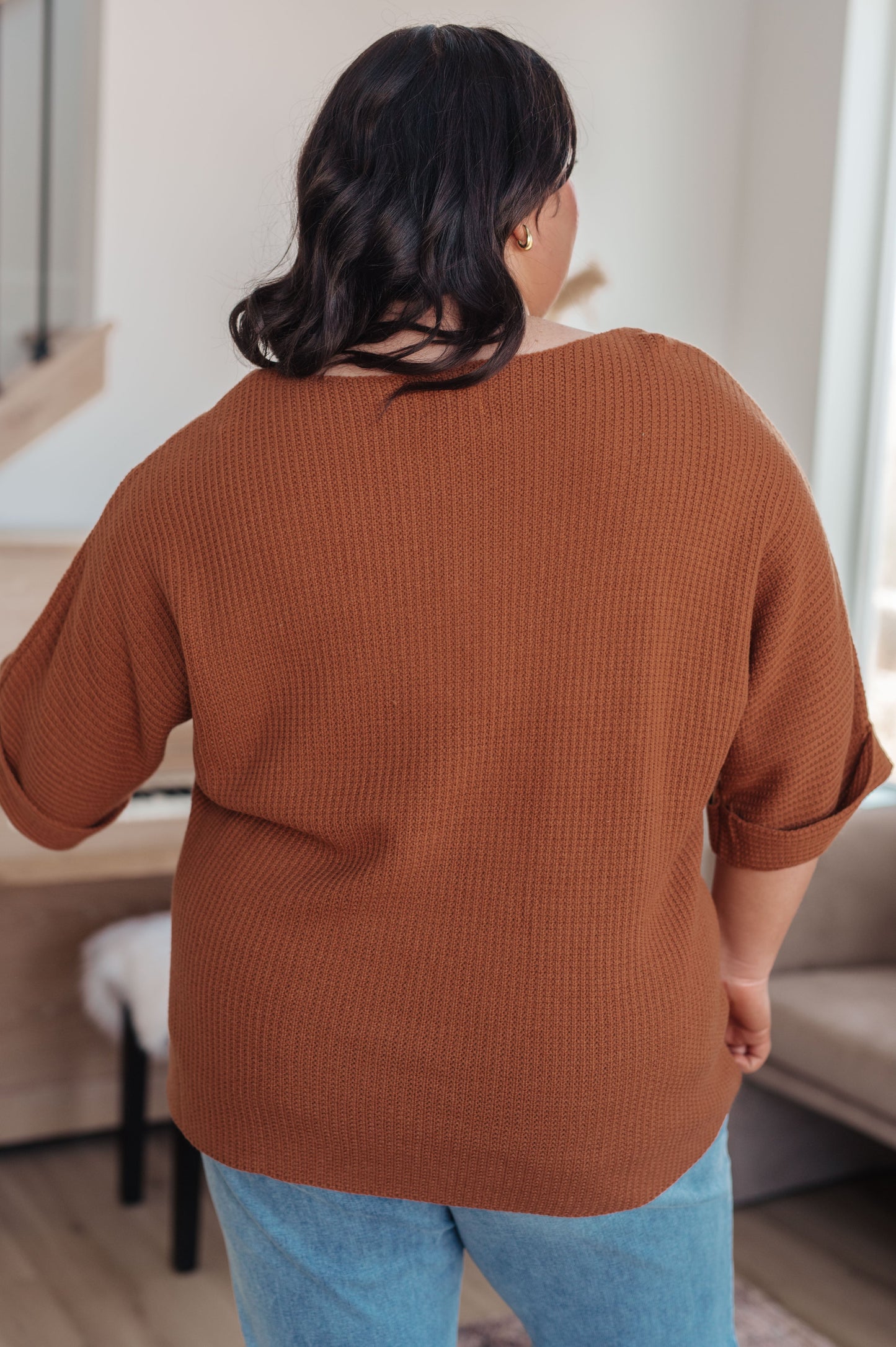 Person wearing a brown sweater and blue jeans in an indoor setting
