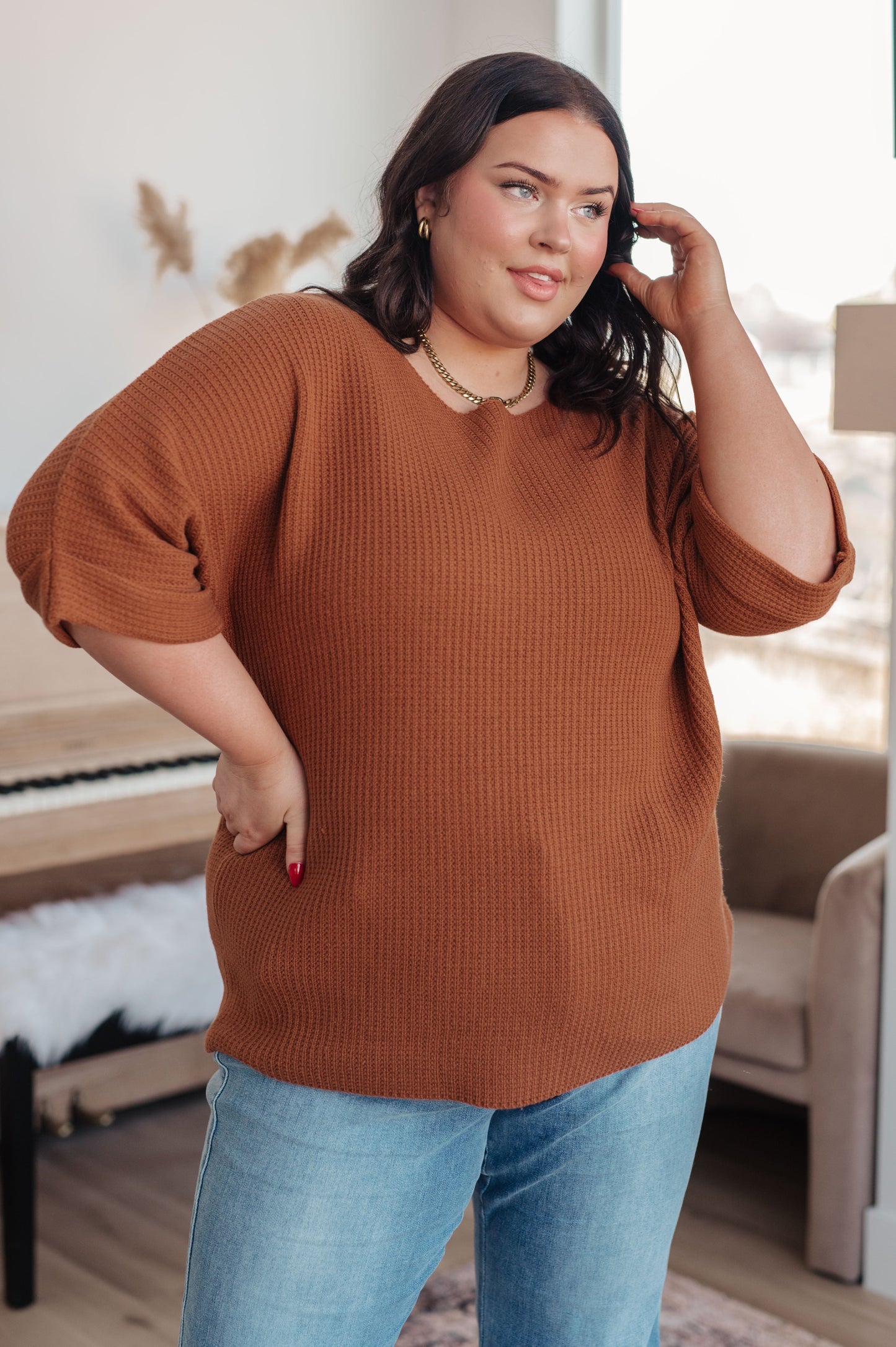Woman wearing a brown sweater and blue jeans indoors