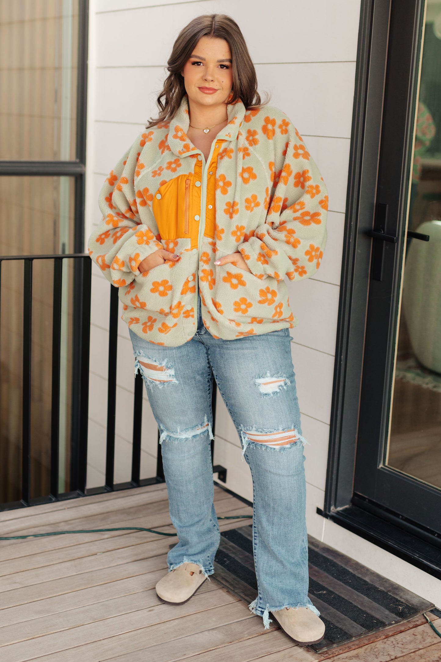 Person wearing a floral jacket and ripped jeans standing on a wooden deck.