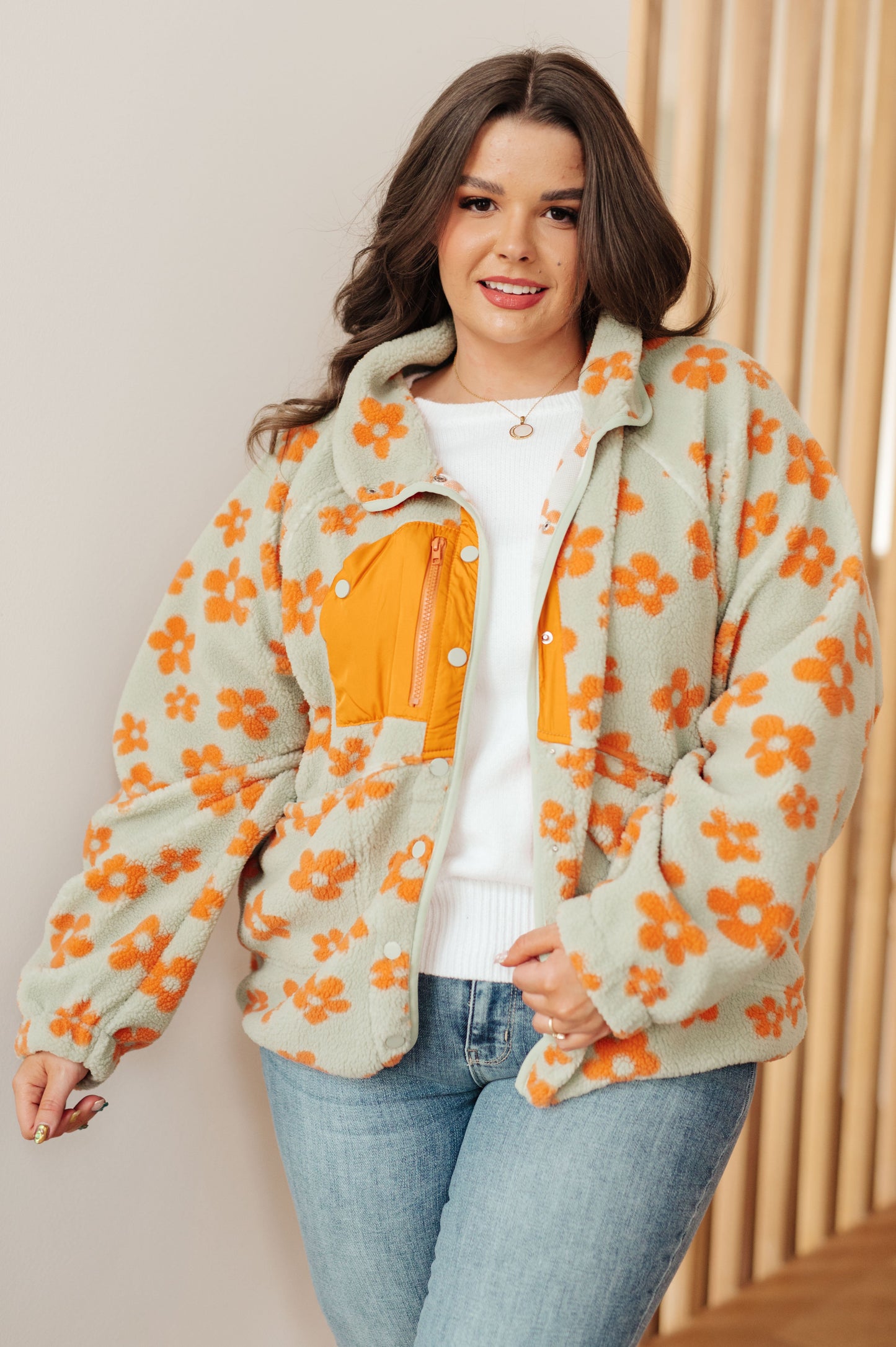 Woman wearing a floral jacket with orange flowers and a white shirt underneath, standing against a neutral background.