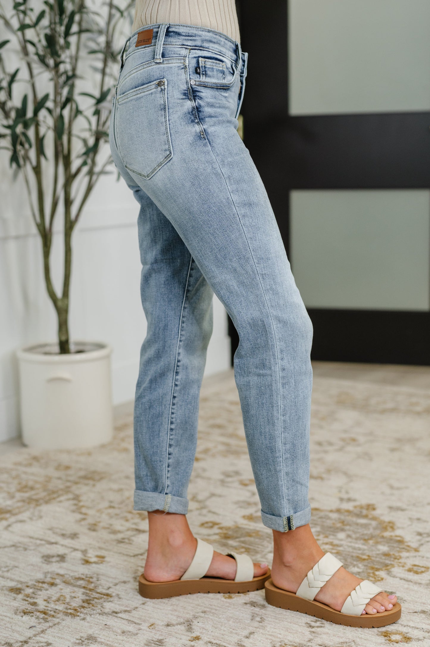 Person wearing light blue jeans and sandals on a neutral background